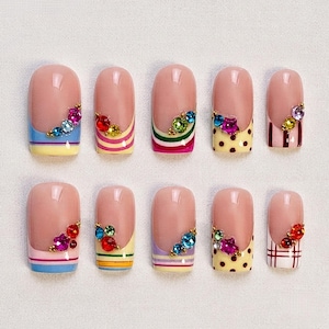May include: A set of ten press-on nails featuring a nude base with various colorful tip designs including horizontal stripes, polka dots, and plaid patterns. Each nail is accented with a cluster of small, multi-colored decorative rhinestones.