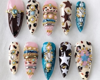 Luxe nepnagels met koeienprint | Nepnagels met luipaardprint en gouden bedeltjes | Stiletto nagels | Coquette Y2K design nagels | Retro jaren 90 nagels