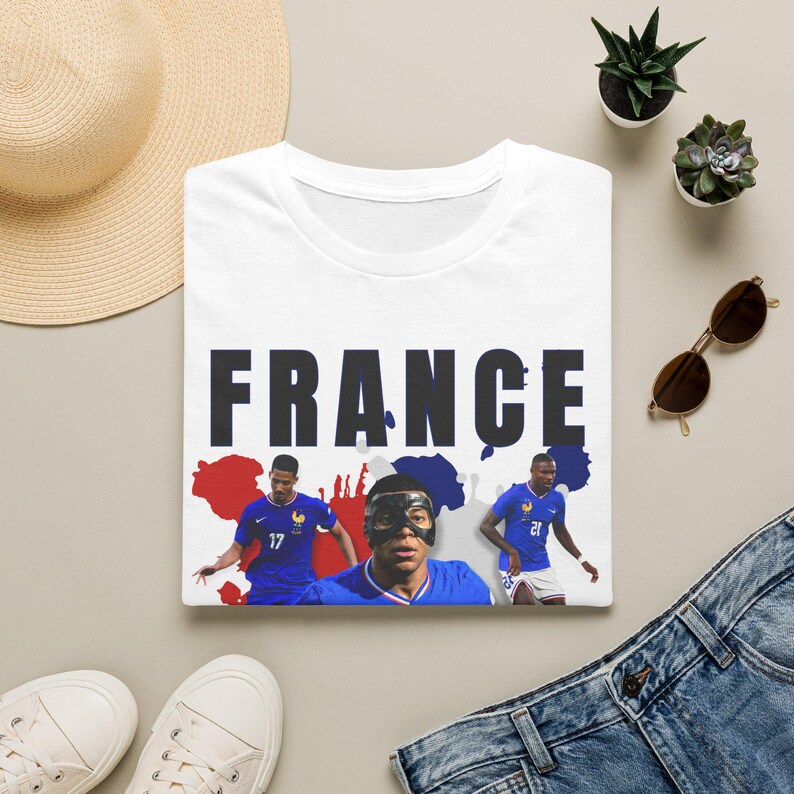 May include: White t-shirt with the word "FRANCE" in large, dark letters. Below the word are images of three soccer players in blue jerseys. The background features a red and blue map outline.