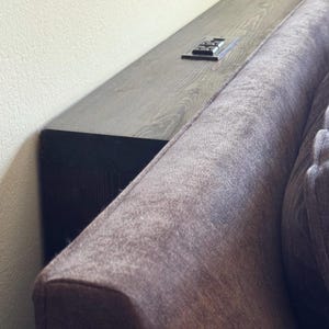 May include: A narrow, dark wood console table positioned behind a dark gray upholstered sofa. The table features a flat, rectangular surface with a visible wood grain texture and an integrated black electrical outlet strip with two power sockets.