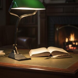 K&ouml;nnte beinhalten: Eine gr&uuml;ne Schreibtischlampe beleuchtet ein offenes Buch und einen Stift auf einem Holzschreibtisch. Die Lampe hat einen dunklen Metallsockel und einen gebogenen Arm. Der Schreibtisch steht in einem Raum mit Kamin und B&uuml;cherregal.