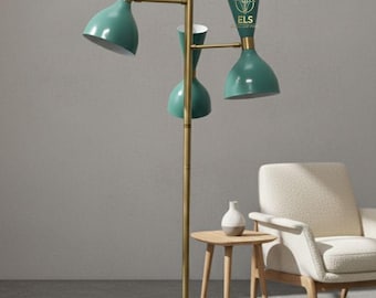 May include: A mid-century modern floor lamp with three teal-colored cone-shaped shades and a brass-colored stem. The lamp has a white marble base. A small wooden side table and a cream-colored armchair are in the background.