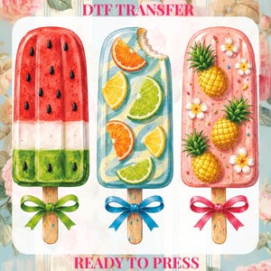 May include: Three colourful popsicle designs. One is watermelon, one has citrus fruits, and the last has pineapples. Each popsicle has a wooden stick and a decorative bow. The text "DTF TRANSFER" and "READY TO PRESS" are visible.