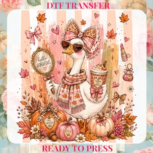 May include: A DTF transfer ready to press featuring a white goose wearing a leopard print bow, heart-shaped sunglasses, and a plaid scarf. The goose holds a mirror with the text hello GORGEOUS and a cup labeled PUMPKIN SPICE PRINCESS near pumpkins.