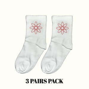 Puede incluir: Dos pares de calcetines tobilleros blancos con un diseño de átomo rojo bordado cerca de la parte superior. El texto "3 PAIRS PACK" está impreso en negro en la parte inferior de la imagen. Los calcetines son de un material suave y cómodo.