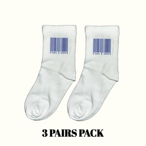 Puede incluir: Dos calcetines tobilleros blancos con un diseño de código de barras azul y los números "2801 | 2026" impresos. El texto "3 PAIRS PACK" está en la parte inferior. Los calcetines se muestran sobre un fondo claro.