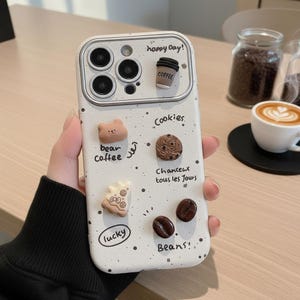 May include: White iPhone case with a coffee and cookie theme. The case features 3D embellishments of a coffee cup, bear, cookie, and coffee beans. Text includes "happy day!", "bear coffee", "cookies", "chanceux tous les jours", "lucky", and "Beans!".