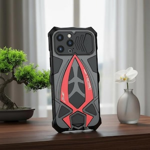 Op de afbeelding: Zwarte, grijze en rode telefoonhoes met een geometrisch ontwerp. De hoes heeft een camerabeschermer en de tekst "FAST & FURIOUS 1". De hoes ligt op een houten oppervlak.