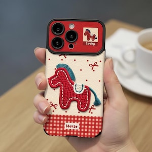 May include: A phone case featuring a red embroidered horse design with a blue mane and tail. The case has a red and white checkered pattern at the bottom and a red camera frame with the word "Locky" and a horse graphic.