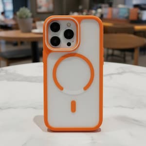 May include: Orange and white phone case with a clear back and orange trim. The case has a circular design on the back and a camera cutout with three lenses. The case is designed to protect the phone from damage.