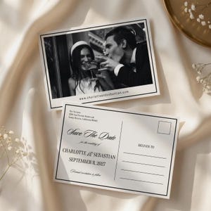 Puede incluir: Postales de boda en blanco y negro de Save the Date. Una postal presenta una foto de una pareja brindando con champán. La otra postal dice "Save the Date" para Charlotte & Sebastian, 11 de septiembre de 2027. También se ve el sitio web www.charlotteandsebastian.com.