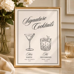 May include: A gold-framed sign with the text Signature Cocktails, featuring a line drawing of a martini glass labeled Hers Martini with vodka, dry vermouth, and olive, and a rocks glass labeled His Old Fashioned with bourbon, bitters, and orange.