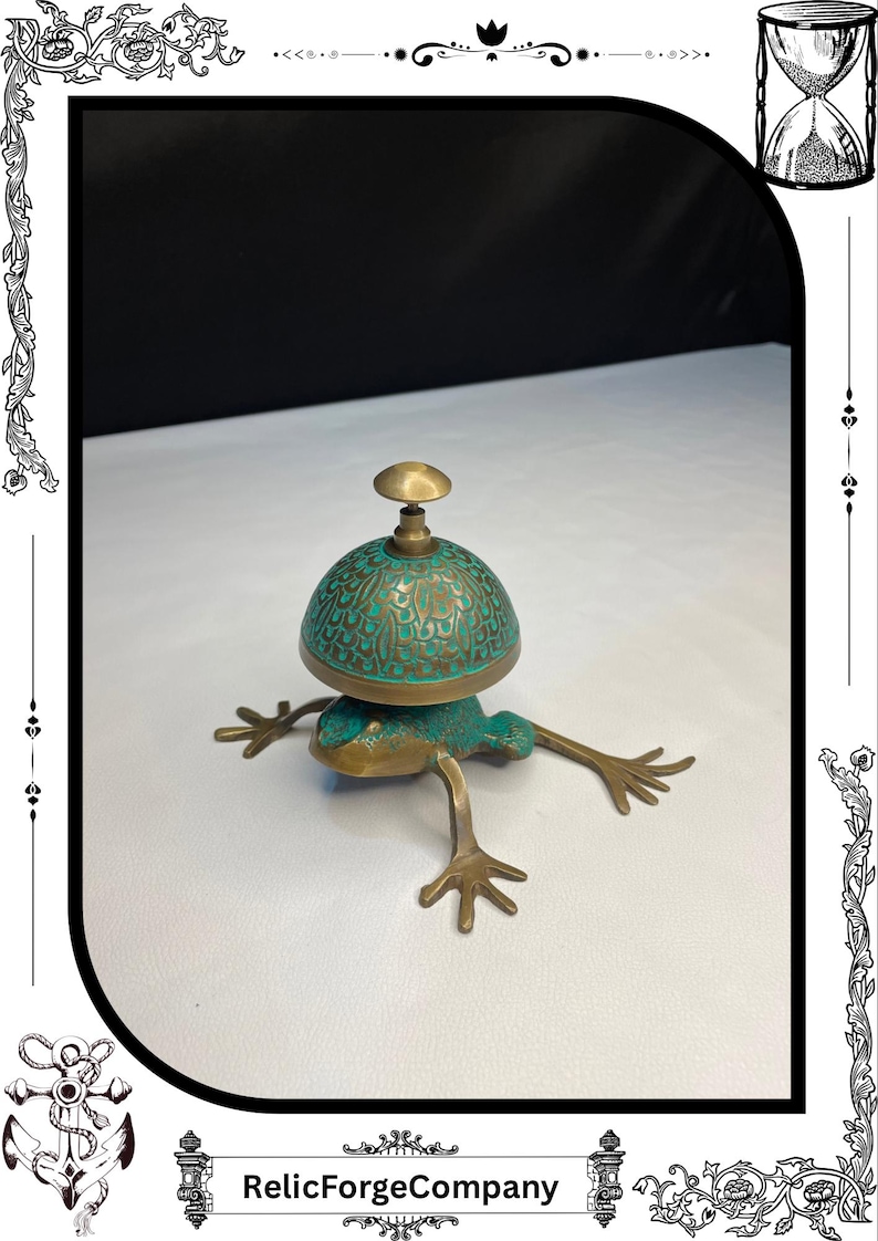 May include: A bronze frog-shaped bell with a turquoise-colored dome-shaped top. The bell has intricate detailing and a small handle. The frog's legs are outstretched, and the bell is resting on a white surface. The text "RelicForgeCompany" is at the bottom.