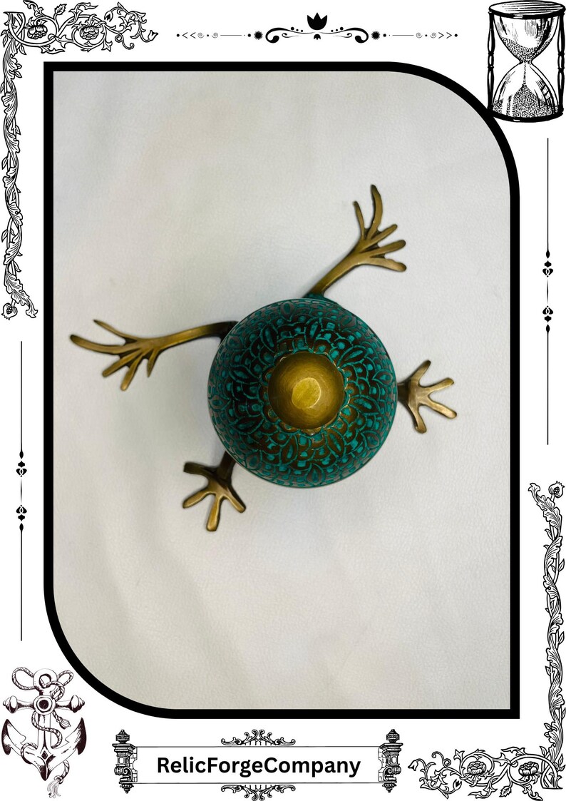 May include: A unique, handcrafted bronze frog sculpture. The frog has a teal-colored, patterned body with a central gold-colored accent. It features outstretched bronze legs and the text "RelicForgeCompany" at the bottom.