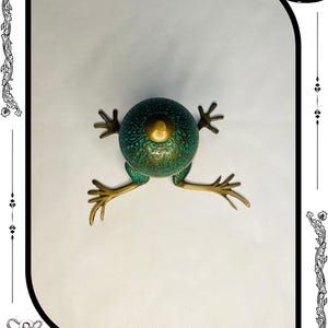 May include: A decorative frog sculpture with a verdigris finish and brass accents. The frog has a round body with intricate patterns and outstretched legs. The sculpture is a unique home decor item.