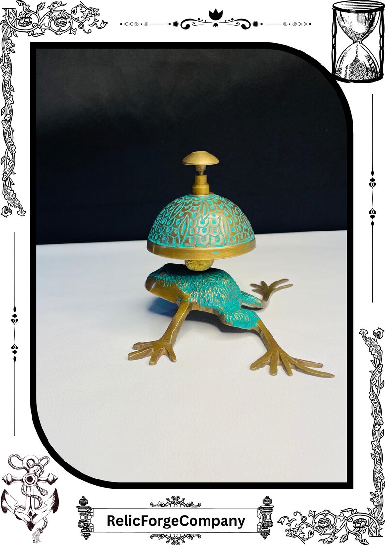 May include: A brass frog-shaped bell with a turquoise and gold dome-shaped top. The bell has intricate detailing and is set against a white and black background. The base of the bell is a frog with outstretched legs.