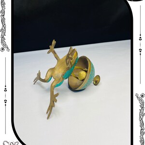 May include: A brass frog figurine with turquoise accents leaps towards a matching bell-shaped container. The container has a detailed pattern and a small handle. The RelicForgeCompany logo is at the bottom.