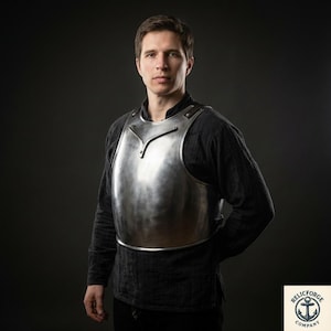 May include: A polished steel breastplate, part of medieval armour, worn over a black long-sleeved shirt. The breastplate has a curved design and is secured with rivets. The image is set against a dark background.