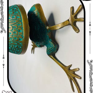 May include: A bronze frog sculpture with verdigris accents. The frog is depicted in a dynamic pose, with outstretched legs and a detailed textured surface. The sculpture has a vintage aesthetic.