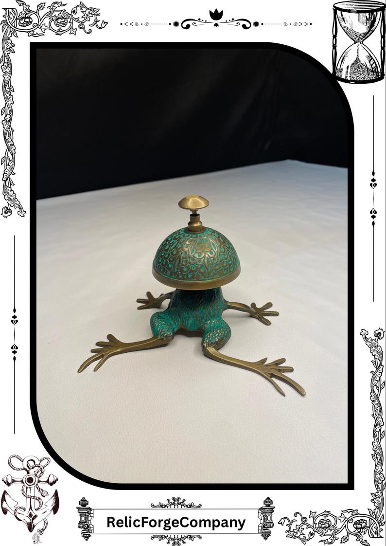 May include: A bronze frog-shaped bell with a green patina and intricate detailing. The bell has a dome-shaped top with a small handle. The frog's legs are outstretched, and the bell is set against a white background.