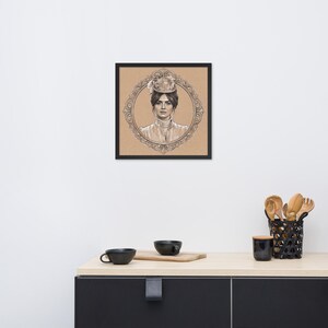 May include: Framed pencil sketch of a woman in a vintage hat and attire, set within an ornate oval frame. The artwork is displayed on a neutral background, encased in a black frame. The image is placed on a light-colored countertop.