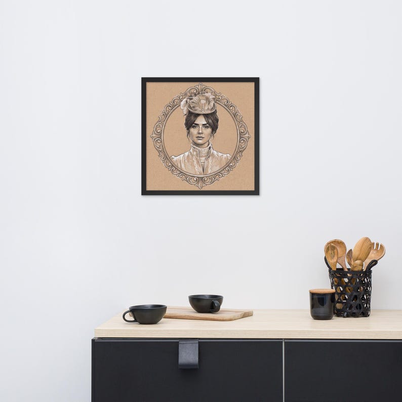 May include: Framed pencil sketch of a woman in a vintage hat and attire, set within an ornate oval frame. The artwork is displayed on a neutral background, encased in a black frame. The image is placed on a light-colored countertop.