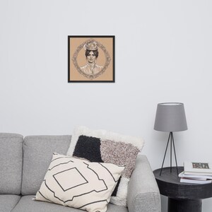 May include: Framed black and white portrait of a woman in a hat, set against a tan background. The portrait is surrounded by an ornate oval frame. The artwork is displayed on a wall above a gray sofa with decorative pillows.