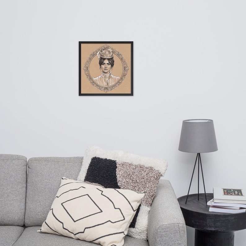 May include: Framed black and white portrait of a woman in a hat, set against a tan background. The portrait is surrounded by an ornate oval frame. The artwork is displayed on a wall above a gray sofa with decorative pillows.