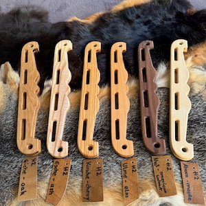 Puede incluir: Seis presas de escalada de madera en varios tonos, incluyendo roble, fresno, cerezo, olmo, nogal americano y arce. Cada presa tiene una forma única con un agarre curvo y varias aberturas rectangulares. Pequeñas etiquetas identifican el tipo de madera.