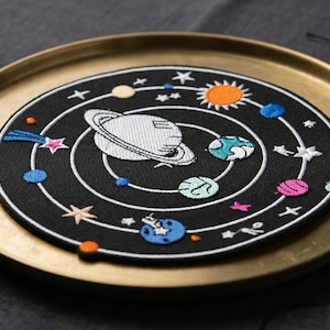 May include: A white ceramic mug with a black handle and the text "But First, Coffee" in a black, bold font. The mug is sitting on a wooden surface. The mug is approximately 4 inches tall.