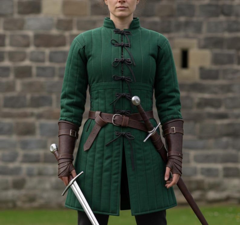 May include: A green quilted medieval tunic with black ties and a brown leather belt. The tunic is paired with brown leather arm guards and a sword. The background features a stone brick wall.