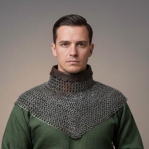May include: A person wearing a medieval chainmail collar over a green tunic. The chainmail is silver-colored and covers the neck and upper chest. The collar is trimmed with brown leather. The background is a neutral gray.
