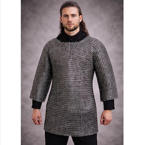 May include: A silver chainmail shirt with long sleeves and a black collar and cuffs. The shirt is made of small, interlocking metal rings and is worn over a black shirt. The garment is designed to protect the wearer.