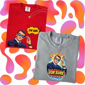 以下が含まれることがあります： 2枚のTシャツ。1枚は赤、もう1枚はグレーで、それぞれサングラスをかけた男性のグラフィックと、漫画風の吹き出しに「FOR SURE」という文字が描かれています。どちらのシャツにもComfort Colorsのタグとネックレスが付いています。