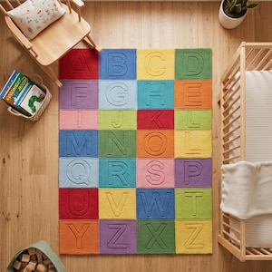 May include: A rectangular area rug featuring a grid of colorful squares, each embossed with a single letter of the alphabet. The rug displays a vibrant palette including red, blue, yellow, green, purple, pink, and orange, arranged in a structured pattern.