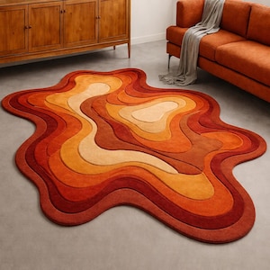 May include: A large, abstract rug with a layered design in shades of orange, red, and beige. The rug has a unique, organic shape, and is placed on a gray floor. The rug's design resembles a topographic map.