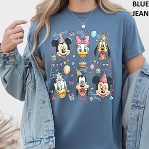 Puede incluir: Camiseta azul con un estampado colorido de personajes de Disney, incluyendo Mickey y Minnie Mouse, Donald y Daisy Duck, Goofy y Pluto, todos con sombreros de fiesta y rodeados de decoraciones de cumplea&ntilde;os. La camiseta tiene la frase "Minnie Mouse XOXO".