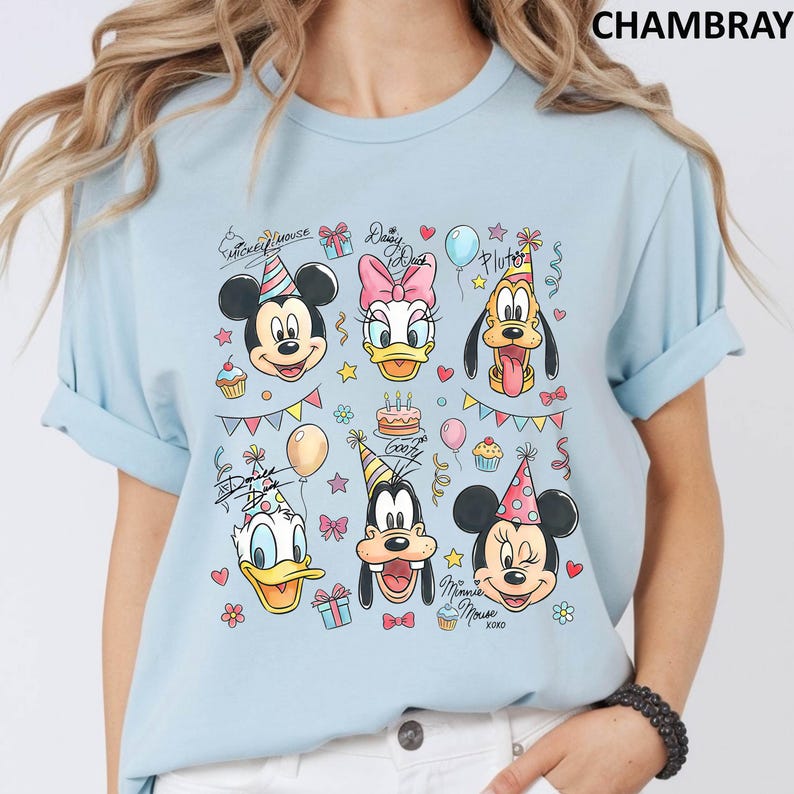 Puede incluir: Camiseta azul claro con un gr&aacute;fico colorido de personajes de Disney, incluyendo Mickey Mouse, Minnie Mouse, Donald Duck, Daisy Duck, Goofy y Pluto. El dise&ntilde;o incluye gorros de fiesta, globos y cupcakes. La palabra "CHAMBRAY" est&aacute; impresa en la parte superior.