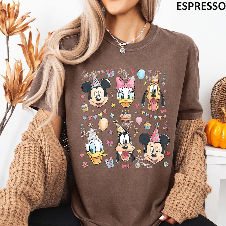 Puede incluir: Camiseta color espresso con un gr&aacute;fico colorido de Mickey Mouse, Daisy Duck, Pluto, Donald Duck, Goofy y Minnie Mouse con sombreros de fiesta. El dise&ntilde;o incluye globos, cupcakes y el texto "Mickey Mouse" y "XOXO".