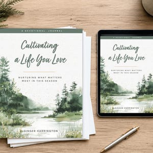 Op de afbeelding: Een devotioneel dagboek getiteld Cultivating a Life You Love door Ginger Harrington, met een aquarellandschap van een rivier en dennenbomen, weergegeven als een fysiek boek en op een tabletscherm naast een zilveren pen.