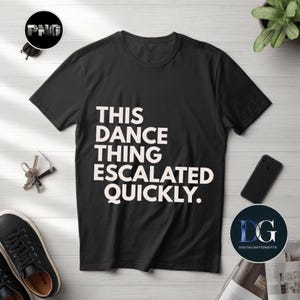 Peut inclure: T-shirt noir avec le texte blanc "THIS DANCE THING ESCALATED QUICKLY." Le t-shirt est présenté sur une surface claire imitation bois, avec des clés, des lunettes de soleil, un téléphone et une plante.