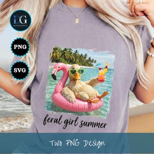 May include: A light purple t-shirt featuring a duck wearing heart-shaped sunglasses and floating on a pink flamingo float in the ocean. The duck is holding a cocktail. Text on the shirt reads "feral girl summer" and "Two PNG Design".
