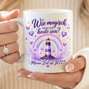 Könnte beinhalten: Weiße Keramik-Tasse mit einem lila-weißen Leuchtturm unter einem Regenbogen, umgeben von lila Herzen und dem deutschen Text "Wie magisch kann ich heute sein?" und "Meine Zeit ist JETZT".