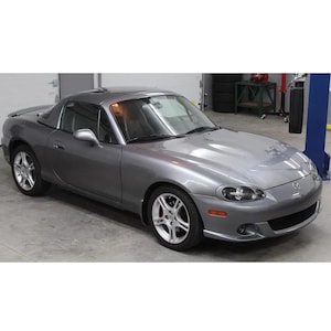 以下が含まれることがあります： グレーのハードトップ付きコンバーチブルスポーツカー。車はシルバーの合金ホイールを備え、ガレージの中に駐車されています。車両は、洗練された空力設計の2ドアモデルです。