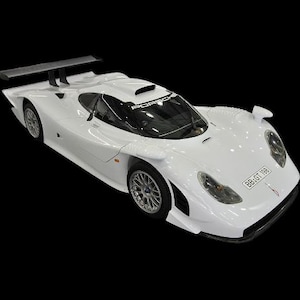 Pode incluir: Um carro desportivo branco com um design elegante, com um spoiler traseiro e elementos aerodinâmicos. O carro tem rodas prateadas e acabamentos pretos, sobre um fundo preto. O veículo parece ser um carro de corrida.