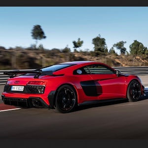 Könnte beinhalten: Ein leuchtend roter Audi R8 Sportwagen auf einer Straße, ausgestattet mit einem schwarzen Heckflügel, schwarzen seitlichen Lufteinlässen, schwarzen Felgen und einem Kennzeichen mit der Aufschrift HN R 8020. Das Fahrzeug hat ein aerodynamisches Design.