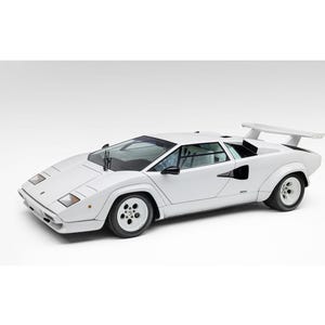 May include: A white Lamborghini Countach sports car featuring a wedge-shaped body, pop-up headlights, a large rear wing, and five-hole alloy wheels. The vehicle is captured from a high-angle side view, showcasing its low profile and angular design.