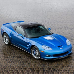 Pode incluir: Um carro esportivo azul brilhante com teto preto. O carro tem rodas prateadas e está estacionado em uma superfície texturizada. O design do carro é aerodinâmico e elegante, com um perfil baixo.