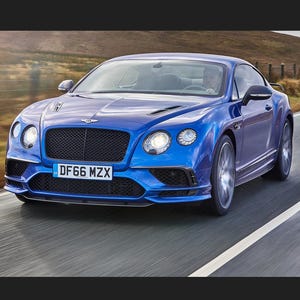Pode incluir: Um cupê Bentley azul a conduzir numa estrada. O carro tem uma grelha preta, faróis e a matrícula diz "DF66 MZX". O carro está em movimento, com um fundo desfocado.