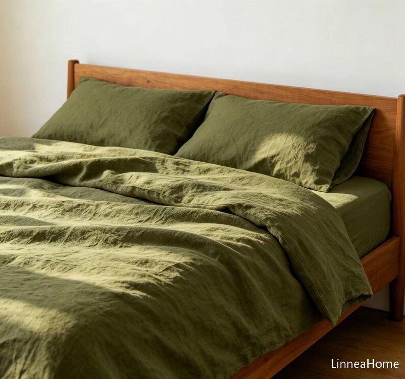 May include: A bed set featuring an olive green duvet cover and two matching pillowcases with a visible textured fabric weave. The bedding is arranged on a wooden bed frame, with the text LinneaHome appearing in the bottom right corner.